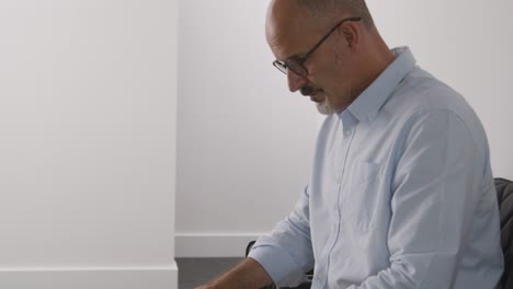 close up of mature man sitting in reception chair for appointment in surgery or hospital waiting room or job interview 2