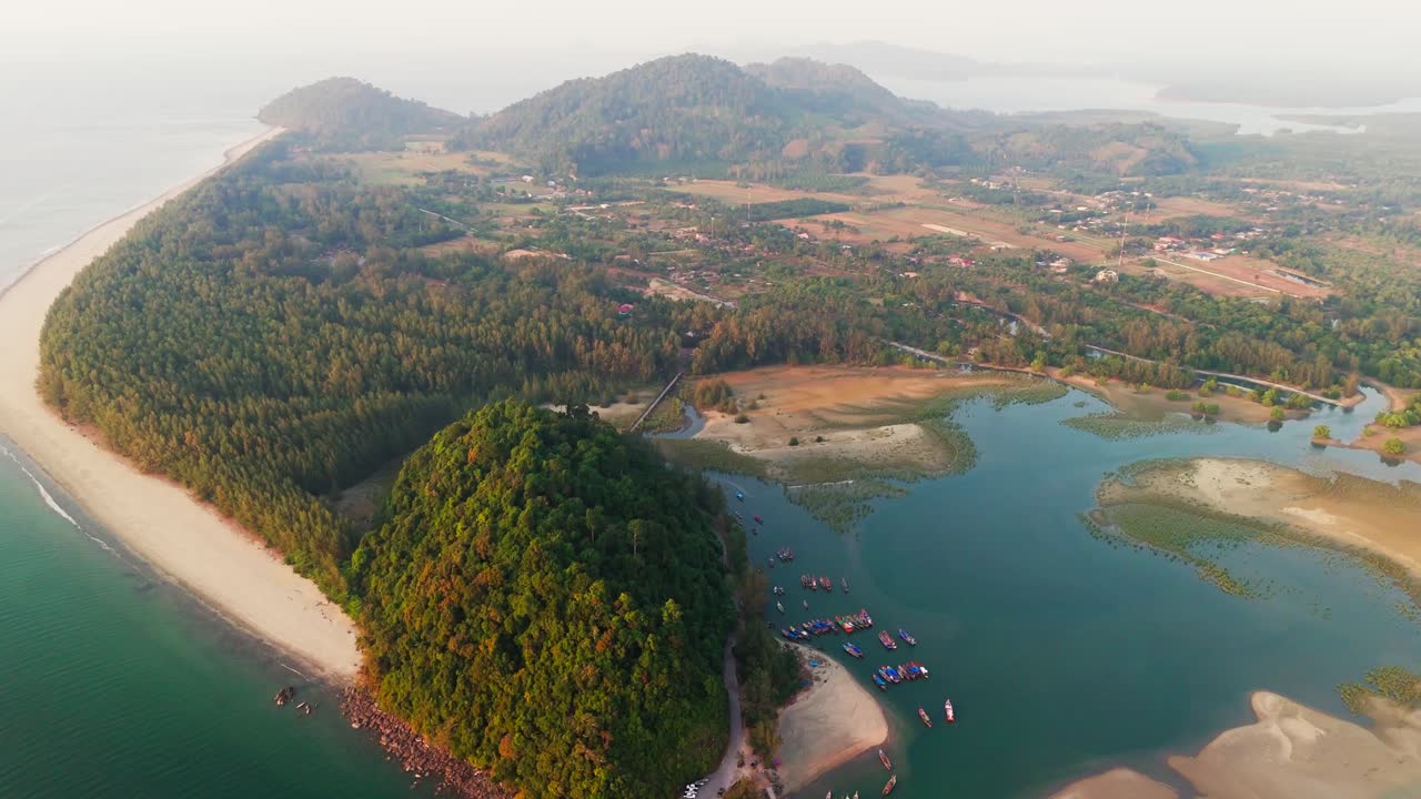 Laem Son National Park in Thailand, drone forward descend shot. Tropical coastline and dense forest from above with sandy beaches meeting lush greenery and a bay with docked boats.
