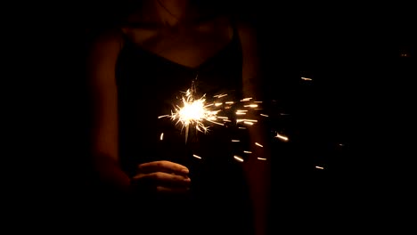 una mujer sostiene un fuego de bengala en su mano. chispas brillan en la oscuridad. mano con un primer plano chispa