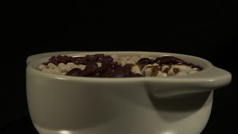 Close-up-side-view:-Bowl-of-dried-beans-revolves-on-dark-background