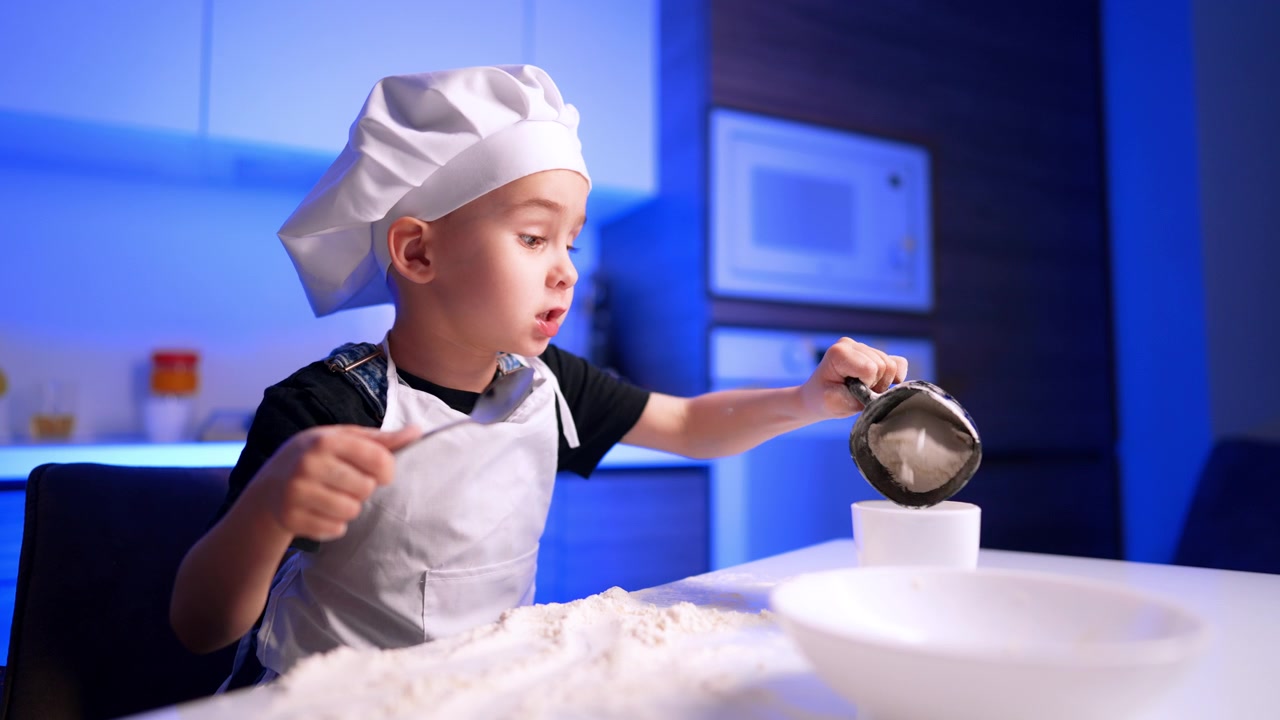 Ragazzo che tiene un cucchiaio e una tazza accanto alla farina. Fotografato di profilo, il bambino guarda in basso vicino a un forno a microonde in una luce blu soffusa.