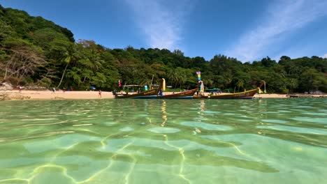 longtail boats float on clear turquoise waters near a lush, tropical beach in phuket, thailand, under bright daylight