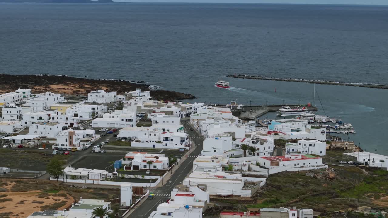 Case bianche tradizionali e porto di Orzola con un traghetto in arrivo a Lanzarote, Spagna. Vista aerea da drone.