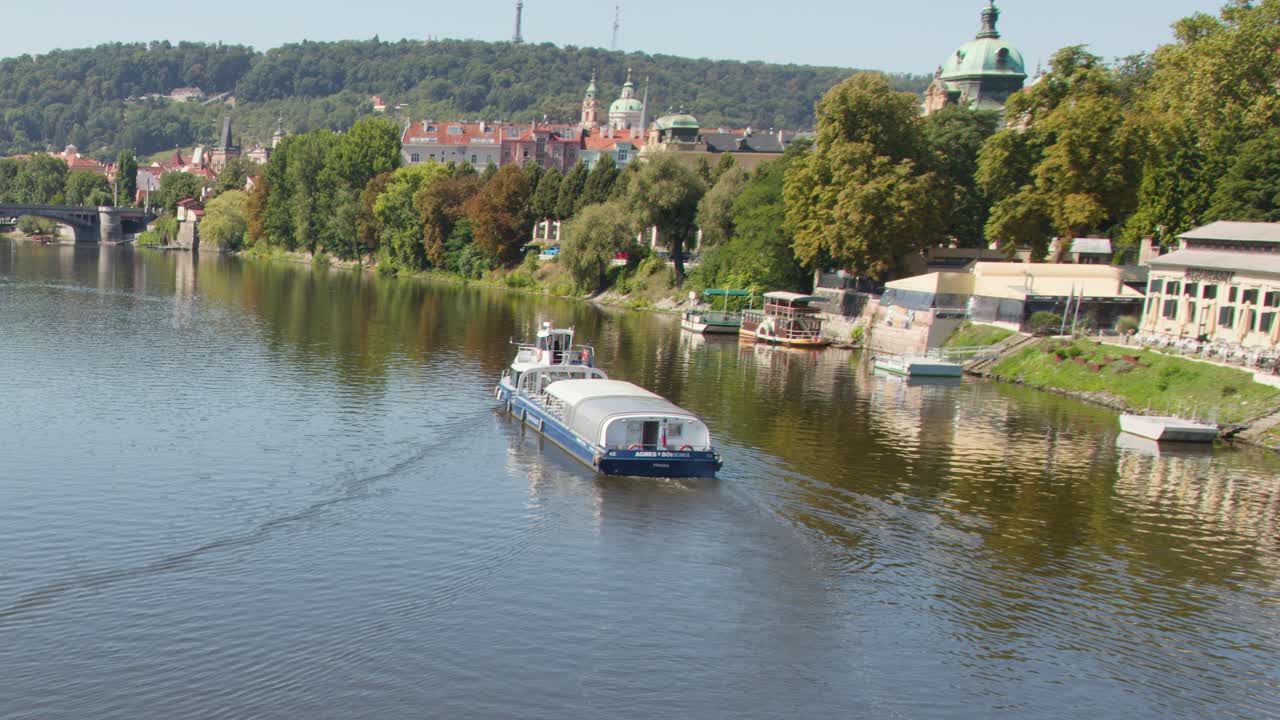Battello passeggeri sul fiume Moldava, Praga, con architettura lungo il fiume, vegetazione e luce del sole estiva