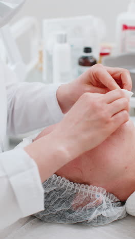 cosmetologist doctor wipes woman face and neck cleaning procedure with cotton wipes in beauty clinic