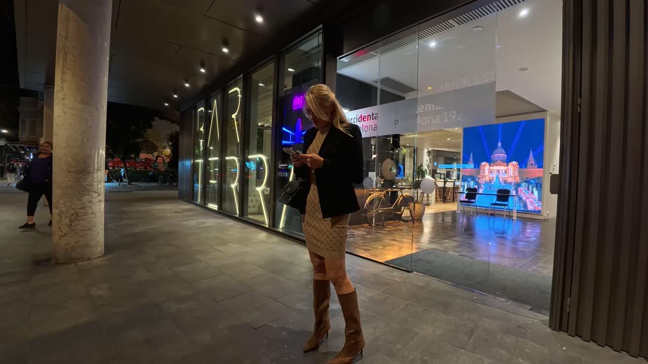 Woman leaving Terra Bar hotel at night while typing on the phone, Barcelona Spain