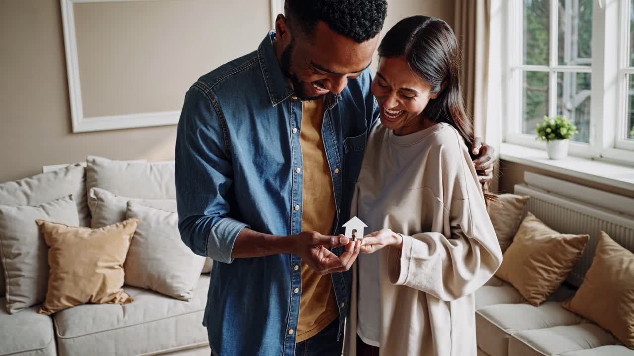 A couple joyfully holding a house model, captured in a cozy living room