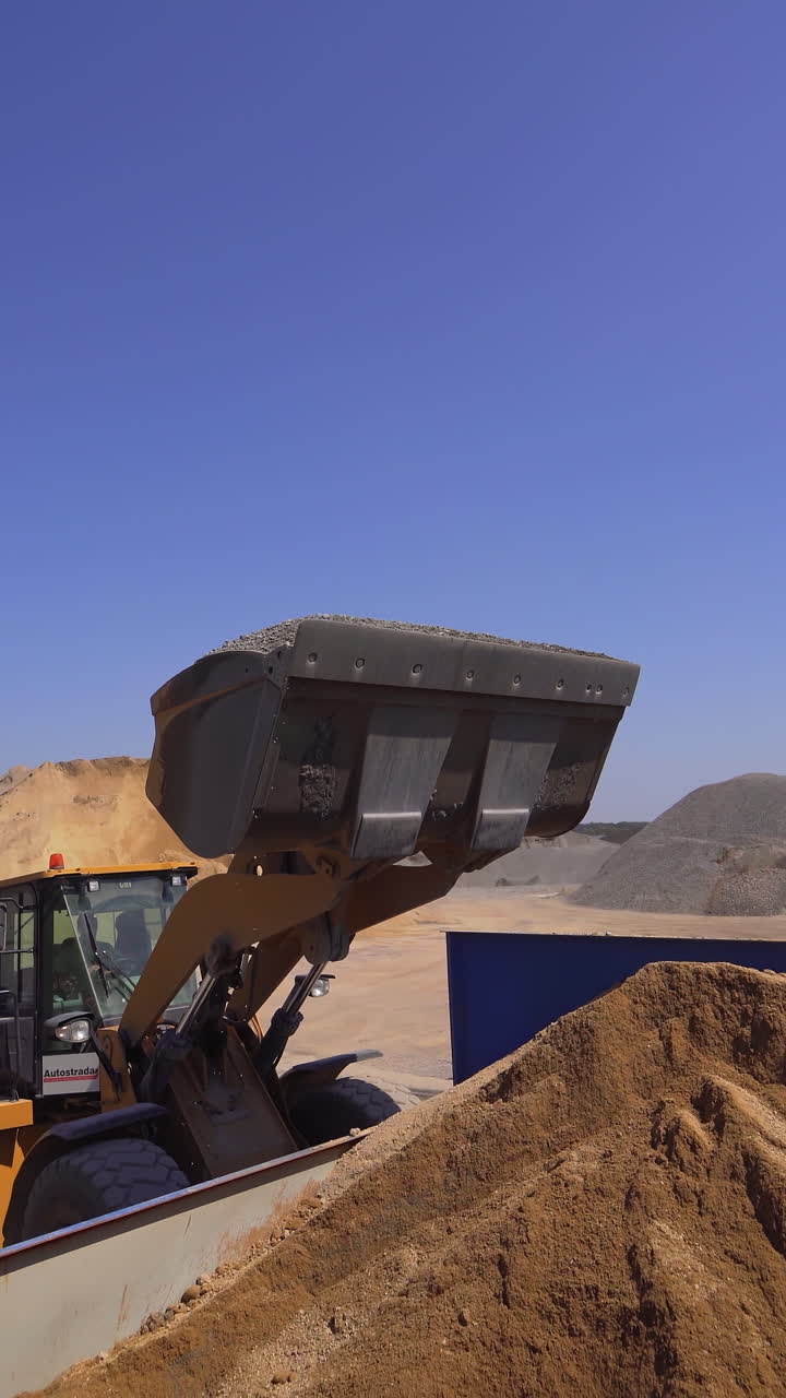 Outdoor plant for making new asphalt. Excavator pouring mixed asphalt. Manufacturing background at daytime. Vertical video