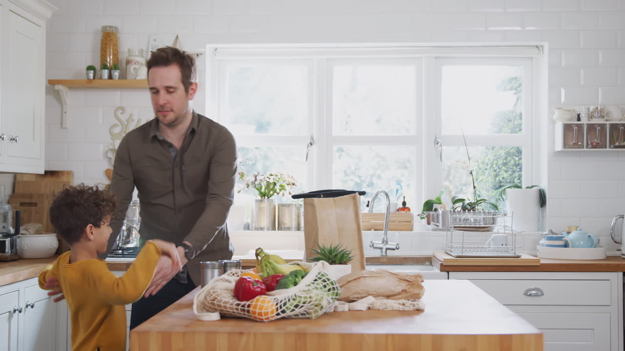 padre e hijo regresan a casa de un viaje de compras usando bolsas de plástico libres desempaquetando comestibles en la cocina