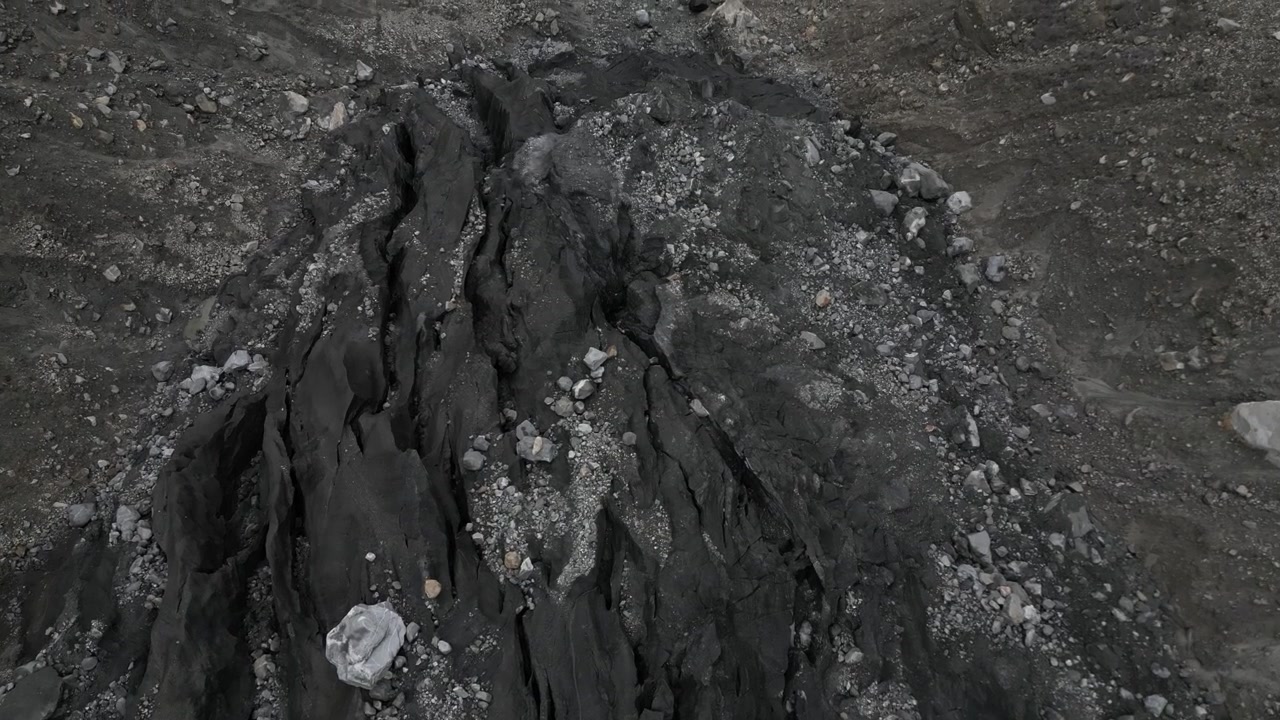 Ripresa ravvicinata con drone in movimento sulle formazioni rocciose scure e fratturate e sui detriti morenici della Valle del Ghiacciaio di Karimabad in Pakistan