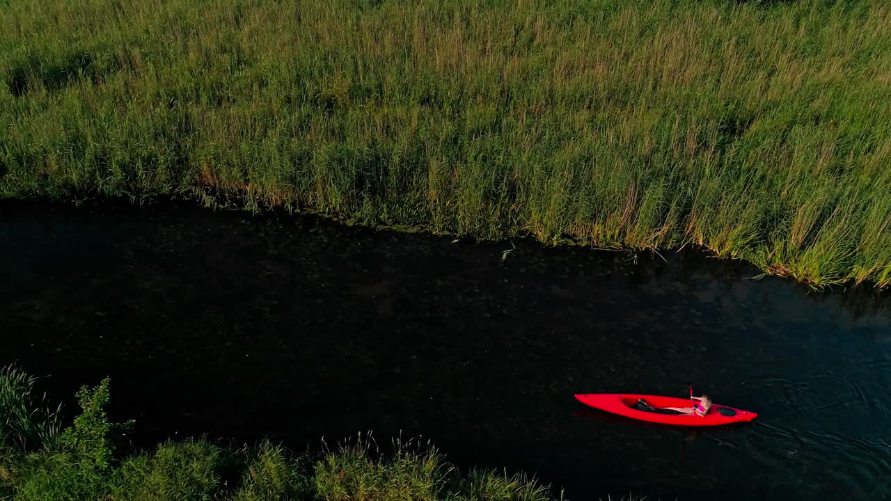 A woman riding a red kayak on a calm river on a warm summer day