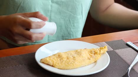 person adding seasoning to a cooked omelette