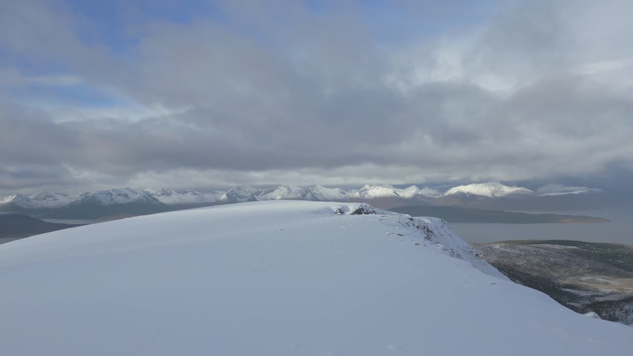 A snow-covered mountain peak overlooking distant snowy ranges under a soft blue sky.