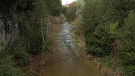 Drone-shot-flying-forwards-across-a-river-gorge-with-clear-running-water,-past-trees-and-rocks