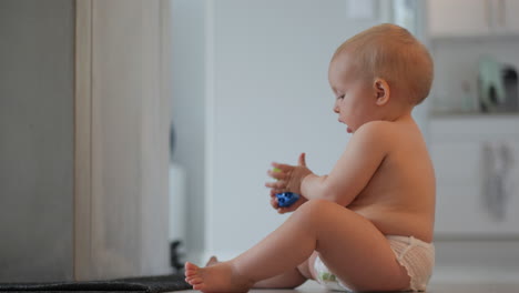 foto de perfil de un lindo bebé caucásico con pañales sentado en el suelo jugando con piezas de plástico