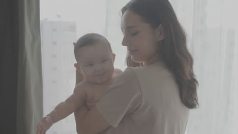 Mamá-Feliz-Con-Su-Lindo-Bebé-En-Sus-Brazos-Mirando-Por-La-Ventana