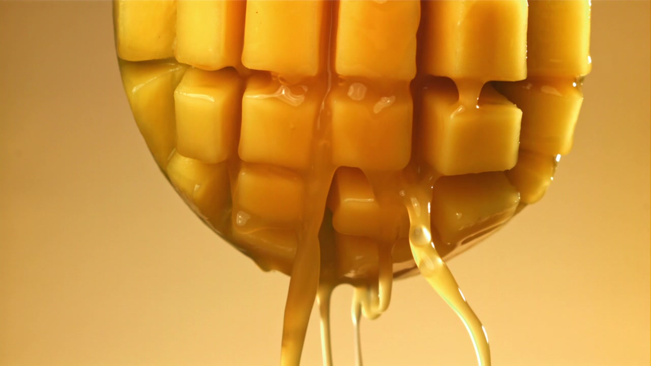 Rallentatore di sciroppo dorato che cola su cubetti di mango fresco