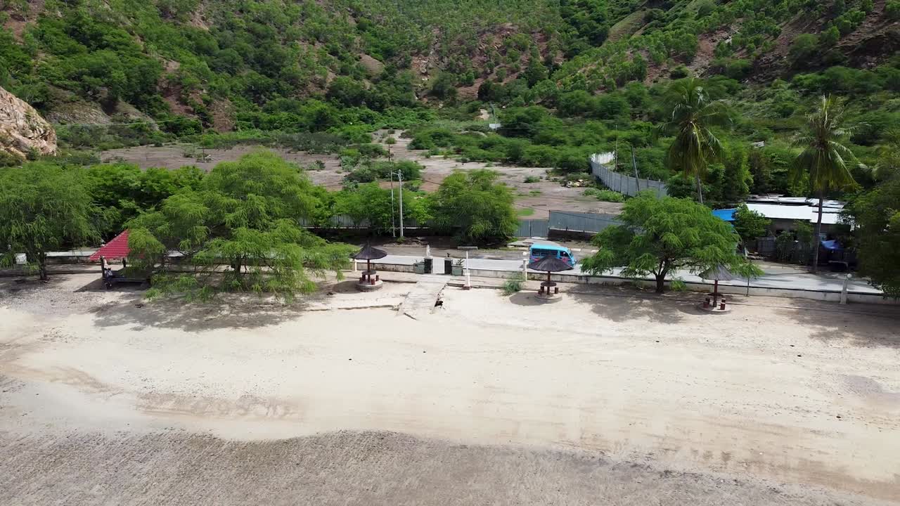 Aerial view of blue microlet local bus driving along coastal road next to white sandy beach in capital city Dili, Timor-Leste, Southeast Asia
