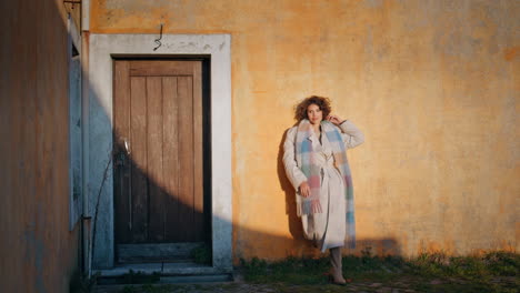 playful woman posing sunlight old wall near rustic door. stylish explorer enjoy