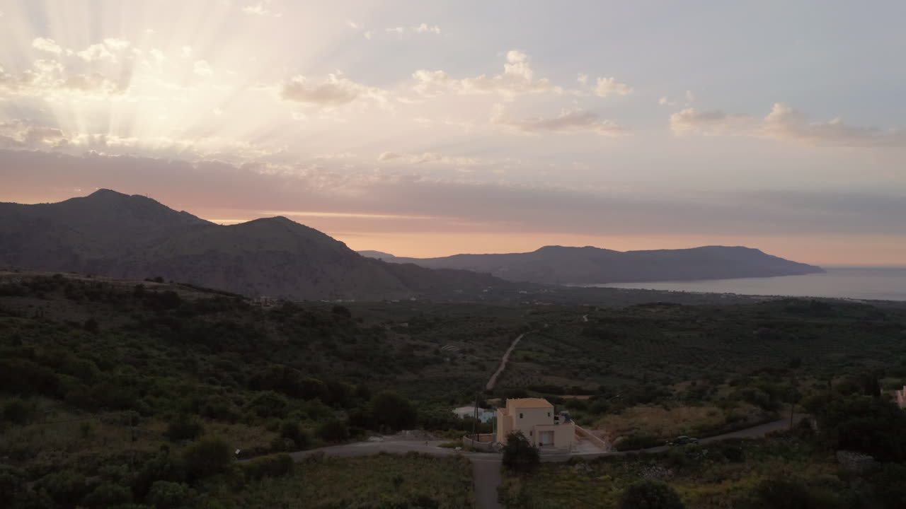 Carrellata aerea delle montagne di Creta, Grecia, al tramonto con bagliori solari e colori caldi e un'auto su stradine di campagna tortuose