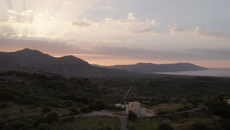 Luftaufnahme-Der-Berge-Auf-Kreta,-Griechenland-Bei-Sonnenuntergang-Mit-Sonneneruptionen-Und-Warmen-Farben-Und-Einem-Auto-Auf-Kurvenreichen-Landstraßen