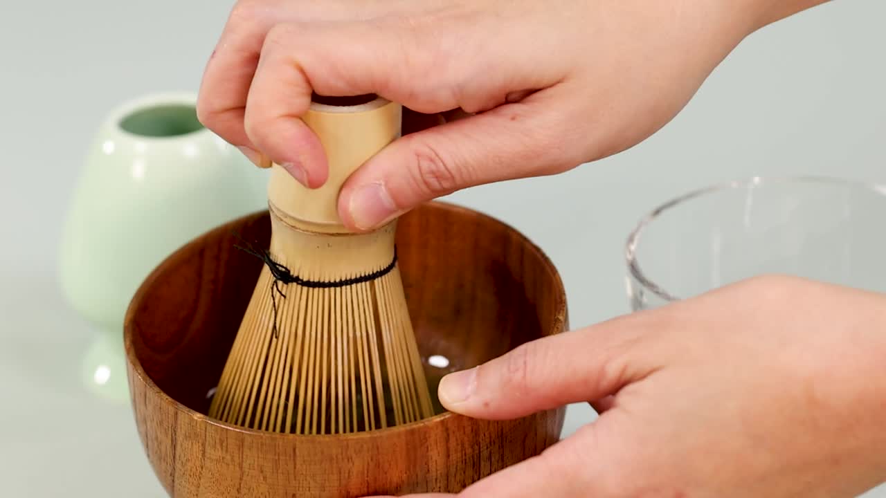Ahşap bir kapta matcha hazırlamak için bambu çırpıcı kullanan ellerin yakın çekim görüntüsü