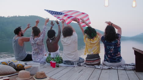 friends sitting on lake pier and swinging us flag