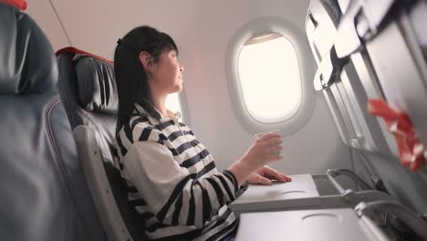 woman sitting inside airplane and looking at window and drinks coffee.