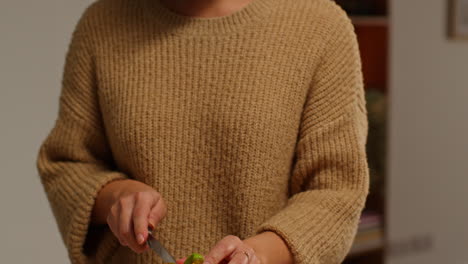 close up of woman at home in kitchen preparing healthy fresh vegetables for vegetarian or vegan meal slicing yellow pepper on board