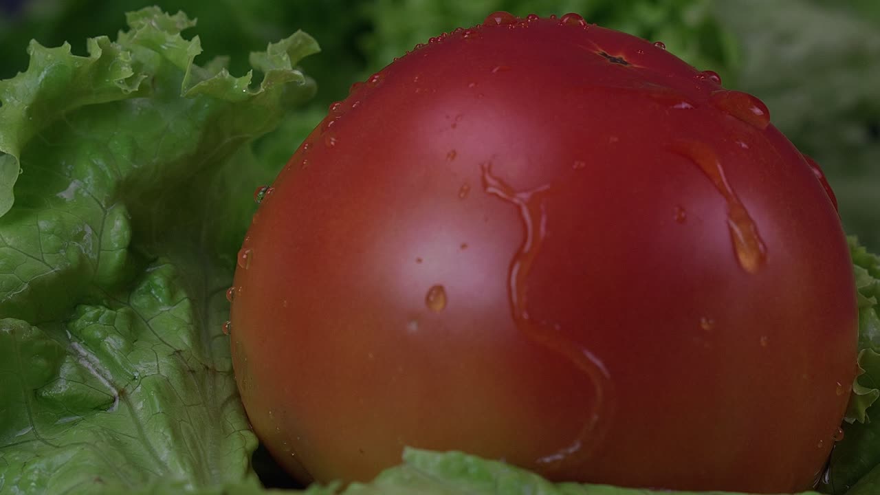 las gotas de agua caen sobre un tomate jugoso y luego se detienen, mientras el tomate gira