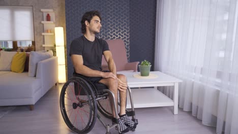 disabled young man is thoughtful and looks out the window of the house.