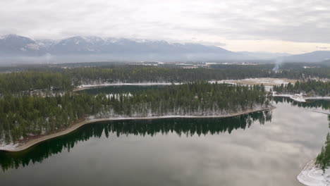 Steigende-Luftaufnahme-Eines-Großen-Sees-In-Der-Wildnis-Von-Montana-Mit-Schneebedeckten-Bergen-Im-Hintergrund