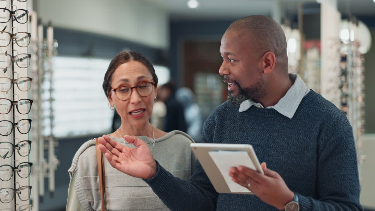 A woman is being helped by a salesperson to choose new eyeglasses at an optical store.