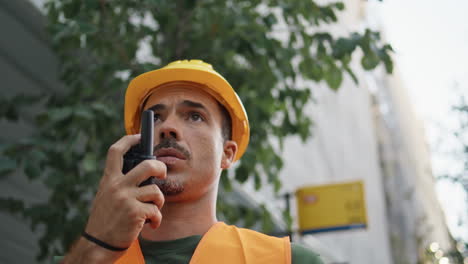 serious builder communicating walkie-talkie stepping city closeup. hardhat man