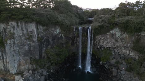 drone aerial view in south korea flying in front of a waterfall over the sea rocky area jeju island
