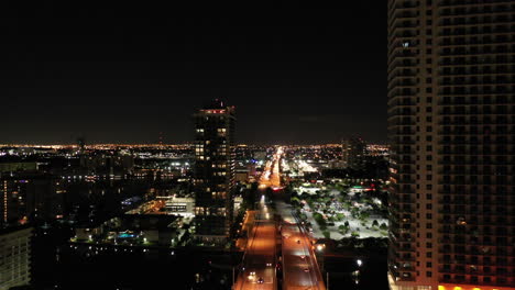 Aerial-night-time-dolly-through-buildings-over-streets-in-Miami