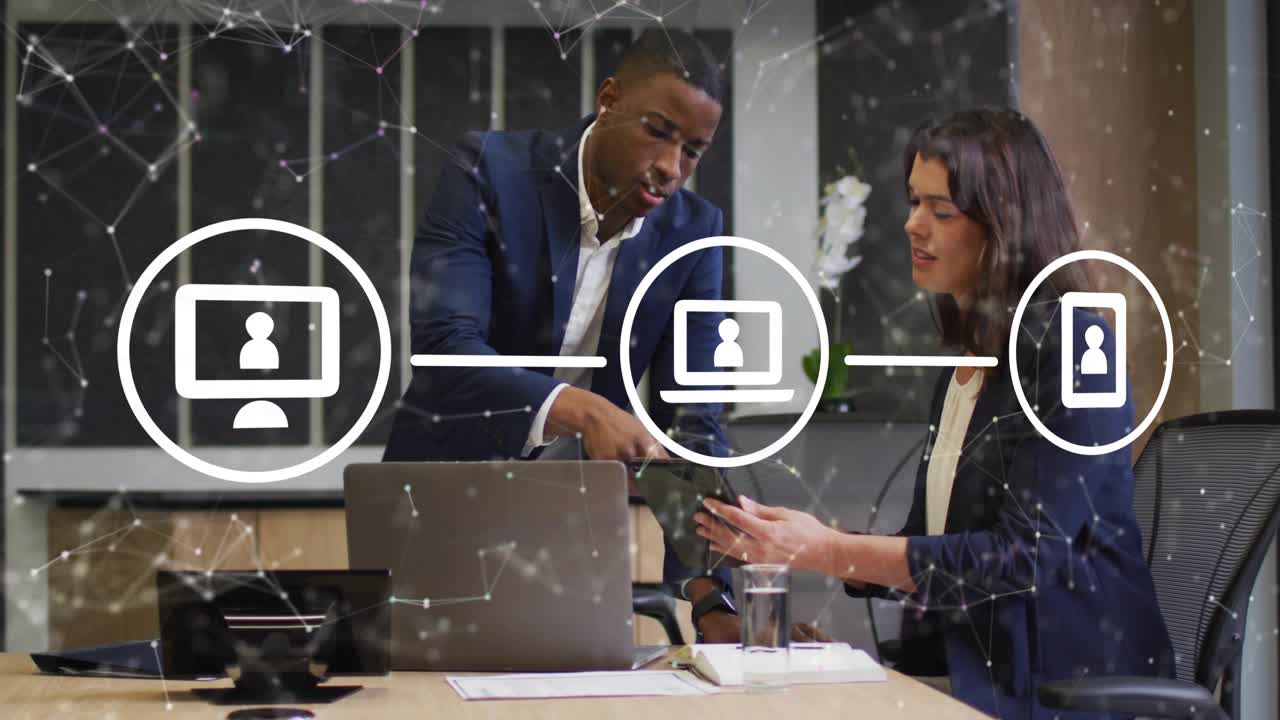 Man leaning, pointing; woman tapping device, network overlay appearing and showing business devices