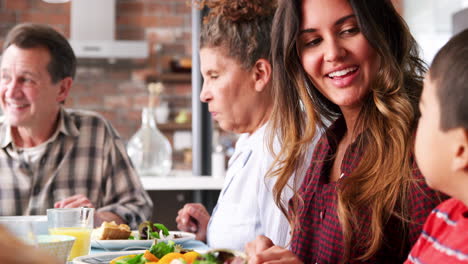 Multi-Generation-Family-Enjoying-Meal-Around-Table-At-Home