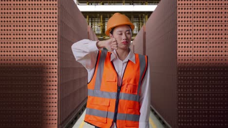 asian female engineer with safety helmet showing thumbs down gesture and shaking her head while standing with red brick packed in stacks are stored