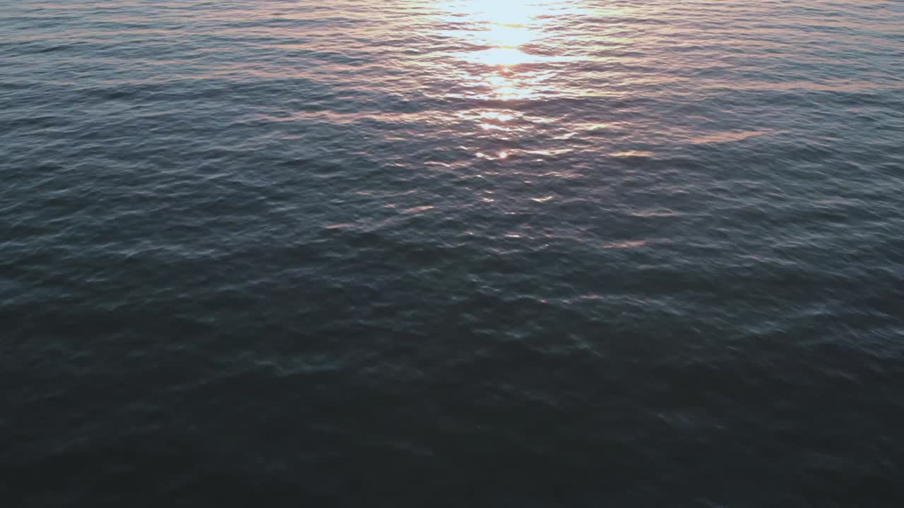 Cinematic aerial video footage flying over calm ocean blue water as view pan up from the sea view to beautiful golden sunset on the horizon while bird fly's over water