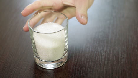 azúcar en vaso. ingredientes para hornear. taza llena de azúcar. mano tomando taza de azúcar