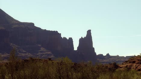 Trucking-right-wide-landscape-shot-of-the-famous-Fisher-Towers-orange-sandstone-natural-rock-formations-with-brush-below-from-a-raft-in-the-Colorado-river-near-Moab,-Utah-on-a-warm-spring-morning