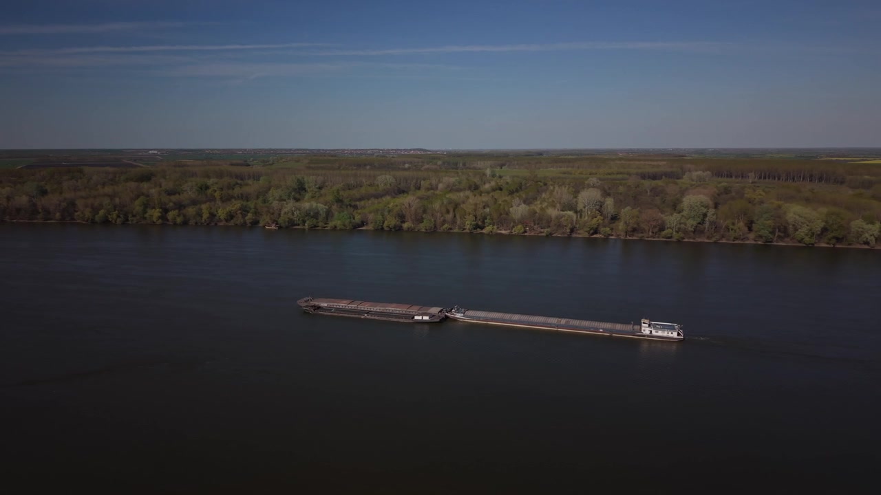 Luftfoto af en fragtpram, der sejler på Donau-floden. Droneoptagelser viser en lang flodfragter på Donau, som er en del af indlandsvandtransporten. Et bredt luftfoto af en kommerciel pram på Donau-floden.