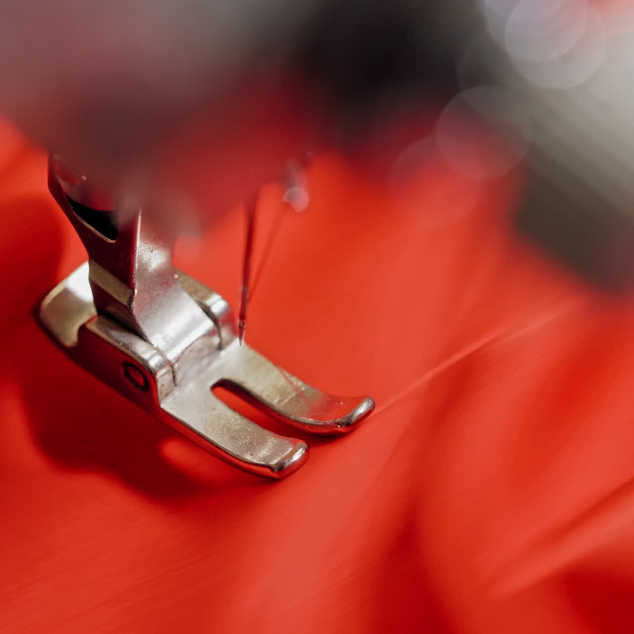 Sewing process on red fabric making a design with a beautiful flower. Hands of seamstress are holding material while working on sewing machine. Close-up.