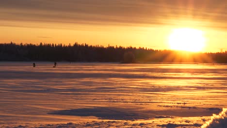 Slider-shot-of-people-ice-fishing,-on-the-frozen-sea,-in-the-Kvarken-archipelago,-at-sunset,-on-a-sunny,-winter-evening,-in-Ostrobothnia,-Finland