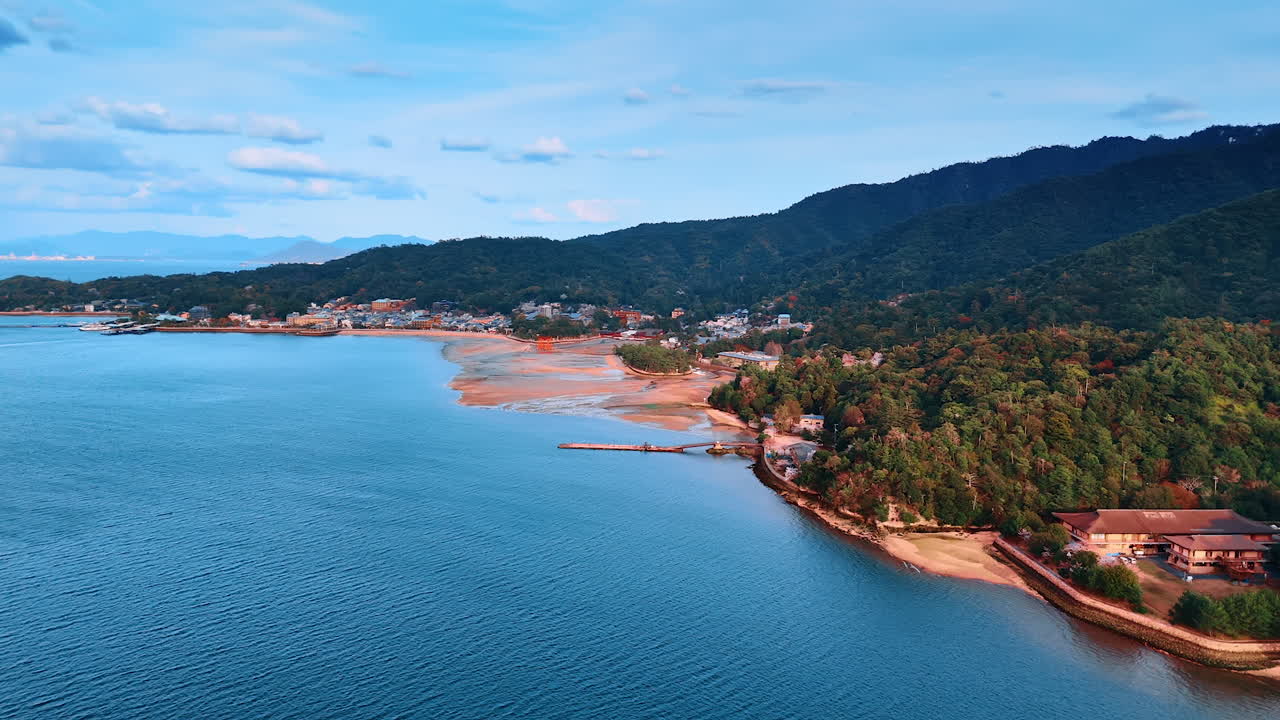 Approaching sandy shore of Miyajima island, Japan with iconic red Grand Torii Gate. Scenic view of the famous landmark and stunning nature from drone footage.