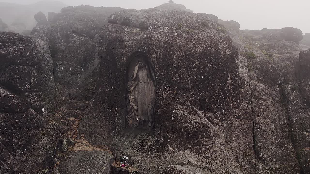 Santuario di Nossa Senhora da Boa Estrela scolpito in un'enorme formazione granitica nella Serra da Estrela, Portogallo, circondato da massi rocciosi e un paesaggio montano nebbioso, ampia inquadratura aerea di ambientazione
