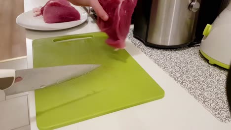 Mujer-Caucásica-Cortando-Carne-De-Cerdo-Con-Un-Cuchillo-Blanco-En-Un-Tablero-Verde