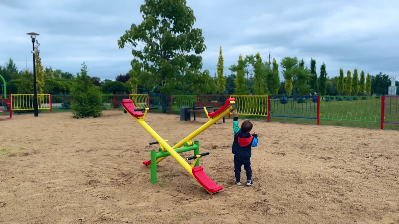 Baby boy plays with seesaw on the playground. Lovely Caucasian toddler outdoors.