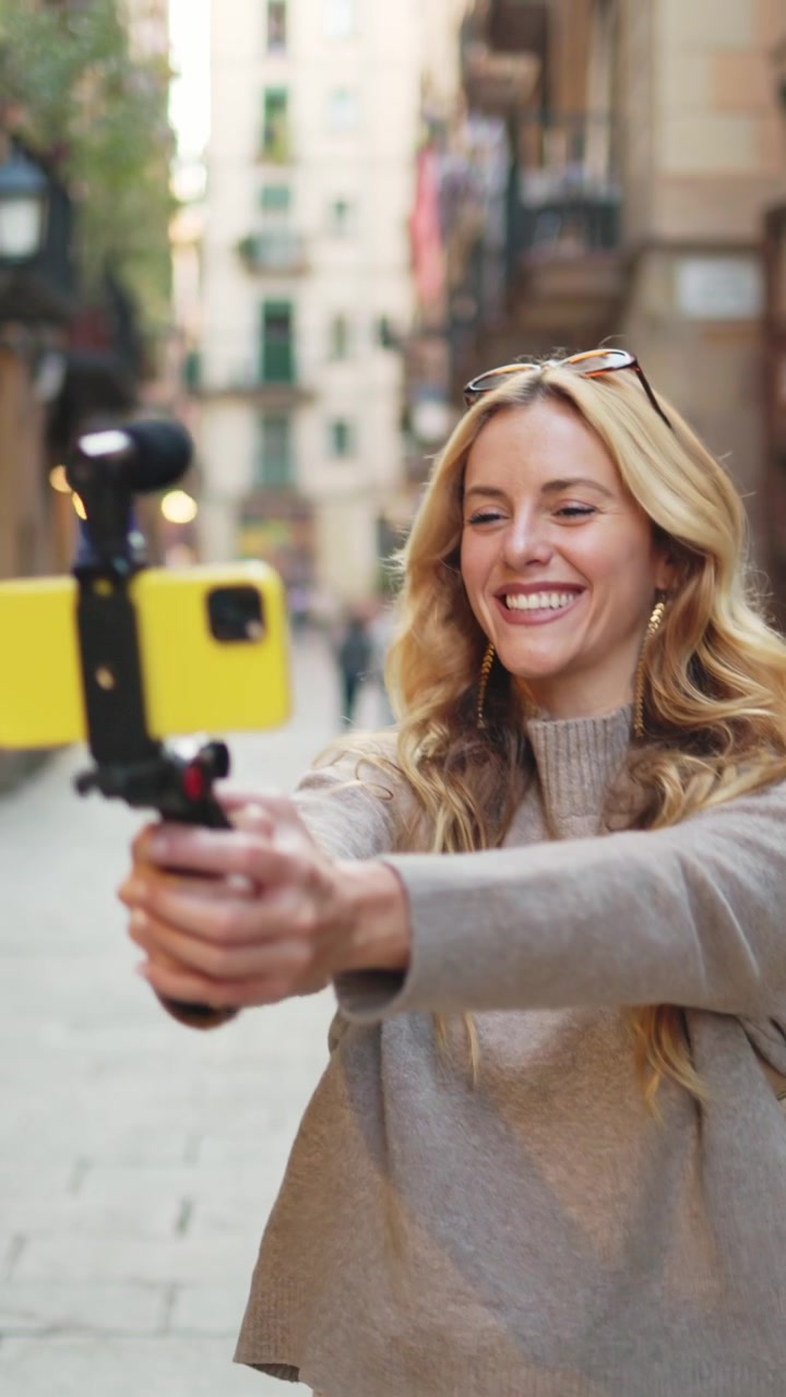 Donna bionda felice che fa vlogging con lo smartphone su una strada cittadina